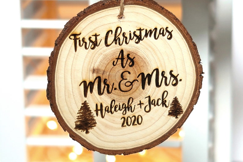 May include: A round wooden ornament with the text "First Christmas as Mr. & Mrs. Haleigh + Jack 2020" and two small pine tree illustrations.