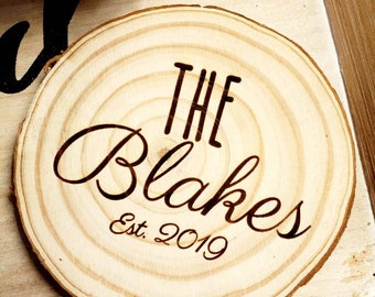 Op de afbeelding: Een rond houten bord met de tekst "The Blakes Est. 2019" gebrand in het oppervlak.