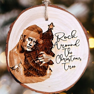 Może przedstawiać: Drewniana ozdoba choinkowa z wypalonym obrazem osoby trzymającej choinkę. Ozdoba ma napis "Rock Around The Christmas Tree".