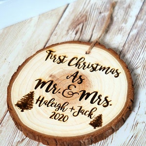May include: A round wooden ornament with the text "First Christmas as Mr. & Mrs.  Haleigh + Jack 2020" and two small pine tree illustrations.
