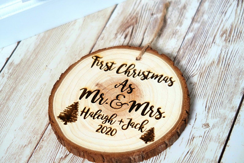 May include: A round wooden ornament with the text "First Christmas as Mr. & Mrs.  Haleigh + Jack 2020" and two small pine tree illustrations.