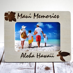 Puede incluir: Un marco de fotos de madera clara con un recorte de una flor de hibisco y una tortuga marina. El marco tiene el texto "Maui Memories" y "Aloha Hawaii" grabado en él. El marco contiene una foto de una familia de cuatro personas caminando por una playa.