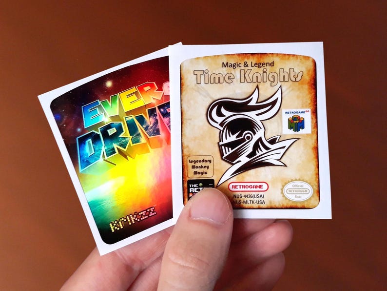 Op de afbeelding: Twee retro game cartridge labels. Het eerste label is voor het spel "Everdrive" met een regenboog achtergrond. Het tweede label is voor het spel "Time Knights" met een ridder in harnas op een bruine achtergrond. De tekst "Magic & Legend" staat boven de ridder.