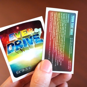 Op de afbeelding: Een sticker met een kleurrijk, 3D-ontwerp van de woorden "Ever Drive" op een achtergrond van een sterrenstelsel met sterren en planeten. De sticker is wit met een zwarte rand en de woorden "Krikzz" zijn onderaan in wit gedrukt.