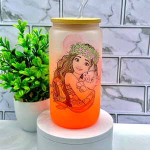 May include: A frosted glass water bottle with a bamboo lid and a straw. The bottle features a colorful illustration of a cartoon character with a pig. The bottle is on a white pedestal.