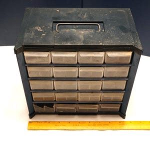 May include: A black plastic storage box with a handle and 18 small drawers. The drawers are clear plastic and are slightly dirty.