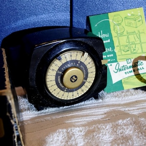 May include: Black vintage Intermatic Time-All timer with a gold-colored dial. The dial has numbers and the words "Evening" and "Afternoon". A green and white instruction manual is behind the timer.