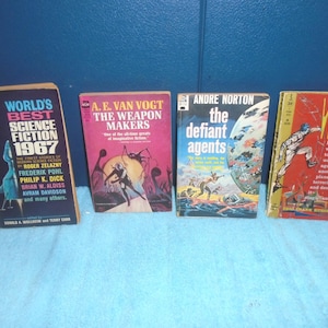May include: Four vintage science fiction books are displayed. Titles include "World's Best Science Fiction 1967", "The Weapon Makers", "The Defiant Agents", and "Wasp". The book covers feature colorful illustrations and text, showcasing classic sci-fi themes.