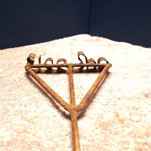 May include: A rusty metal tool with the words "The Shoe" embossed on the top. The tool has a triangular shape with three legs and a long handle.