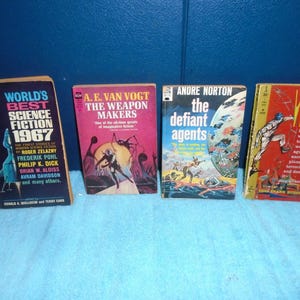 May include: Four vintage science fiction paperback books lined up. Titles include World's Best Science Fiction 1967, The Weapon Makers by A.E. Van Vogt, The Defiant Agents by Andre Norton, and Wasp by Eric Frank Russell, featuring colorful cover art.