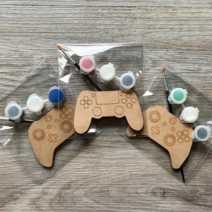 Peut inclure: Kits de peinture de manettes de jeu à faire soi-même. Chaque kit comprend une manette en bois, des pots de peinture de différentes couleurs et un pinceau. Les manettes ont la forme de manettes de jeu classiques.