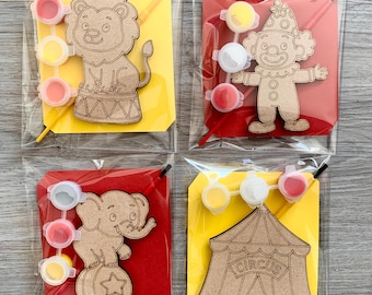 May include: Four paint-your-own circus-themed kits. Each kit includes a wooden cutout of a lion, clown, elephant, or circus tent, paint pots, and a paintbrush. The kits are packaged in clear plastic bags with yellow or red backing.