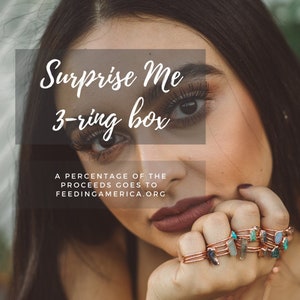 May include: Image features a woman with long eyelashes and dark hair, wearing multiple copper-toned rings adorned with gemstones. Text overlay reads "Surprise Me 3-ring box." Additional text states that a percentage of proceeds goes to FeedingAmerica.org.