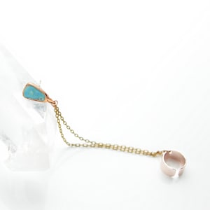 May include: A gold ear cuff with a turquoise stone pendant hanging from a chain.