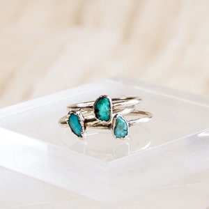 May include: Three silver rings with turquoise stones set in the center of each ring. The rings are stacked on top of each other on a clear acrylic platform.