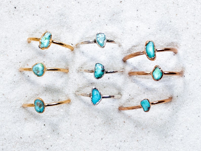 May include: A set of nine rings with turquoise stones. The rings are made of gold and silver and feature different shapes and sizes of turquoise stones.