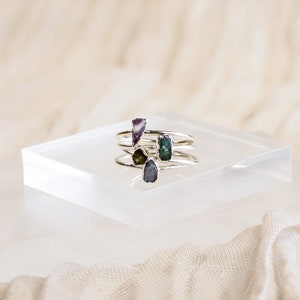 May include: Four silver rings with different colored gemstones. The rings are stacked on top of each other on a white surface.