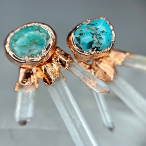 May include: A pair of earrings featuring turquoise stones set in rose gold with clear quartz crystals hanging from the bottom.
