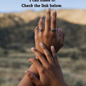 May include: Two hands with rings on the fingers. The rings are made of copper and have green stones. The background is a blurry image of a mountain range.