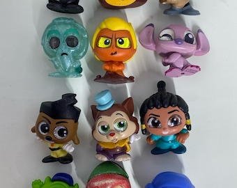 May include: A collection of twelve small, stylised character figurines featuring various colours and designs, including figures with glittery textures, a blue lightsaber, a top hat, and large expressive eyes, arranged in a four-by-three grid.