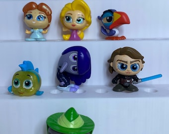 May include: A collection of ten small, stylised plastic character figurines featuring various animated and cinematic figures, including a green-clad character with glasses, a blue-clad figure with a lightsaber, and several colourful animal and human characters.