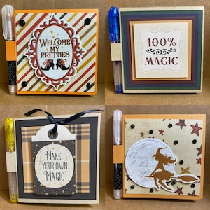 May include: Four small, square notebooks with attached pens. Each notebook features a different design with text: "Welcome My Pretties", "100% Magic", "Make Your Own Magic", and a witch on a broom. The notebooks have decorative borders and embellishments.