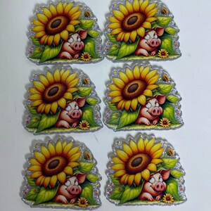 May include: Six identical flat acrylic charms featuring a cartoon pig peeking out from under a large yellow sunflower with green leaves. Each charm has a glittery border and a die-cut shape, showcasing a pig with a pink snout and wide eyes.