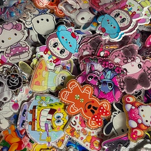May include: A collection of assorted acrylic character charms featuring various cartoon figures including Hello Kitty, SpongeBob SquarePants, Stitch, and a gingerbread man. Each charm has a glossy finish with glitter accents and vibrant colours.