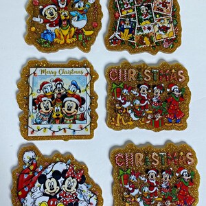 May include: Six glittery gold resin ornaments featuring Disney characters in holiday attire. Designs include Mickey, Minnie, Donald, Goofy, and Pluto in various Christmas scenes, some with the text Merry Christmas or CHRISTMAS.