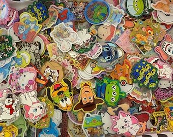 May include: A large collection of assorted colorful stickers featuring various cartoon characters, including Disney, Pixar, and classic animation figures. The stickers have diverse shapes, glittery textures, and vibrant printed designs.