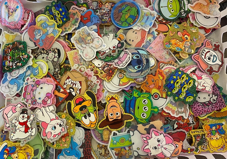 May include: A large collection of assorted colourful stickers featuring various cartoon characters, including Disney, Pixar, and classic animation figures. The stickers have diverse shapes, glittery textures, and vibrant printed designs.