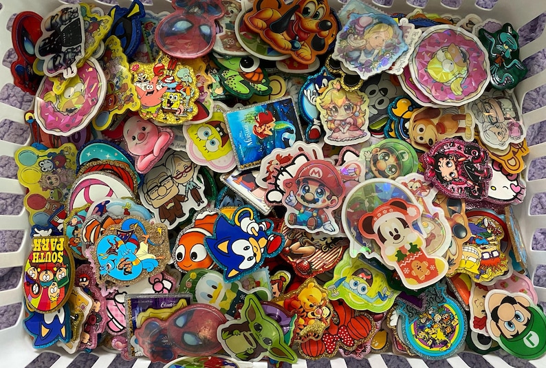 May include: A large collection of assorted colourful stickers featuring various cartoon characters, pop culture icons, and animated figures. The stickers vary in shape and size, displaying vibrant illustrations with holographic and glittery finishes.