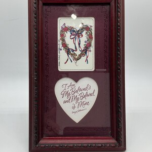 May include: A rectangular dark red wooden frame containing two white inserts. The top insert features a heart-shaped floral wreath illustration with ribbons. The bottom heart-shaped insert displays the text I Am My Beloved's and My Beloved is Mine.