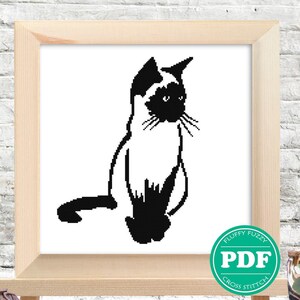 May include: Black and white cross stitch pattern of a Siamese cat sitting with its tail curled behind it. The pattern is framed and displayed on an easel.