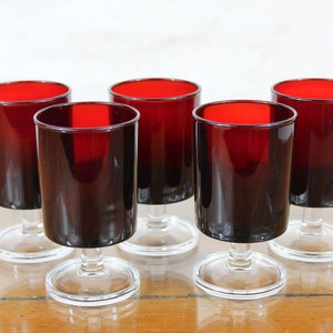 Puede incluir: Juego de seis vasos de vidrio rojo con tallo. Los vasos son transparentes con un tinte rojo oscuro y tienen un diseño simple.