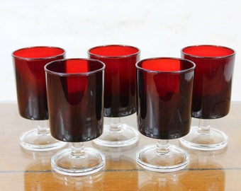 May include: Set of six red glass stemmed drinking glasses. The glasses are clear with a dark red tint and have a simple design.