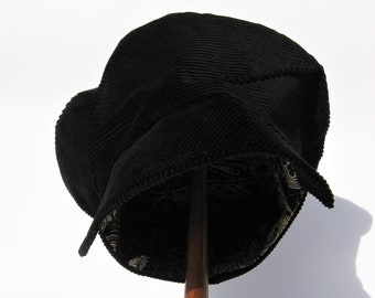 May include: A black corduroy hat with a patterned lining, displayed on a wooden stand.
