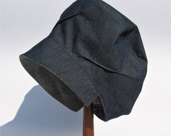 May include: A denim hat with a folded brim, displayed on a wooden stand. The hat is dark blue and has a plaid lining visible at the brim.