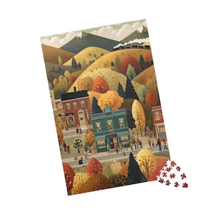 May include: A colorful jigsaw puzzle depicting a quaint autumn town scene. The puzzle features buildings, trees with fall foliage, a train, and mountains in the background. A few puzzle pieces are scattered at the bottom.