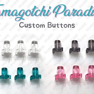 May include: An assortment of custom buttons for Tamagotchi devices. The image displays clear, gray, teal, and pink buttons. The text "Tamagotchi Paradise" and "Custom Buttons" are visible.