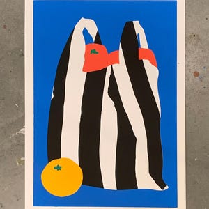 May include: Abstract art print featuring a black and white striped bag with red and green shapes inside, set against a vibrant blue background. A yellow orange sits at the bottom left corner. The artwork is framed with a white border.