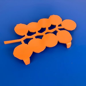 Op de afbeelding: Een oranje metalen onderzetter in de vorm van een tak met ronde bladeren.