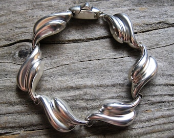 May include: A silver bracelet with a wavy, leaf-like design. The bracelet is made of polished metal and has a clasp closure.