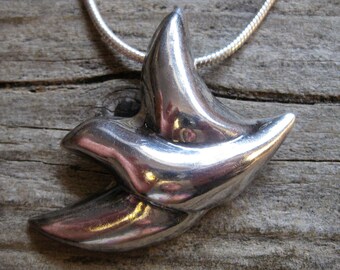 May include: A silver pendant necklace featuring a stylized bird design. The pendant is made of smooth, polished metal and has a contemporary look.