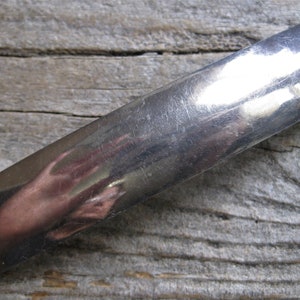 Op de afbeelding: Een rechthoekige, zilverkleurige metalen haarspeld met afgeronde randen. De haarspeld reflecteert de omgeving en vertoont een licht bekrast oppervlak. Het haaraccessoire ligt op een verweerde houten achtergrond.
