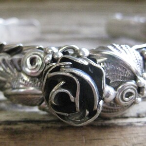 May include: A silver bracelet with a black rose design. The bracelet is intricately detailed with swirls and leaves.