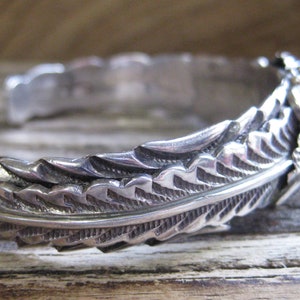 May include: A silver bracelet with a detailed feather design. The bracelet is made of sterling silver and has a delicate, intricate design.