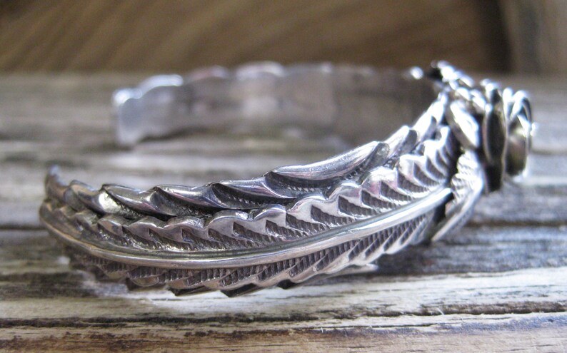 May include: A silver bracelet with a detailed feather design. The bracelet is made of sterling silver and has a delicate, intricate design.