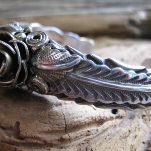 May include: A silver bracelet with a detailed rose design and a textured leaf pattern.