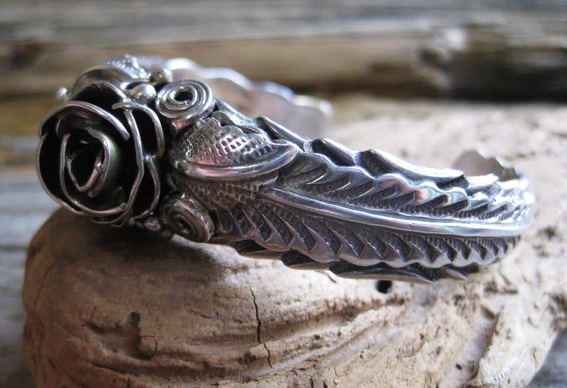 May include: A silver bracelet with a detailed rose design and a textured leaf pattern.